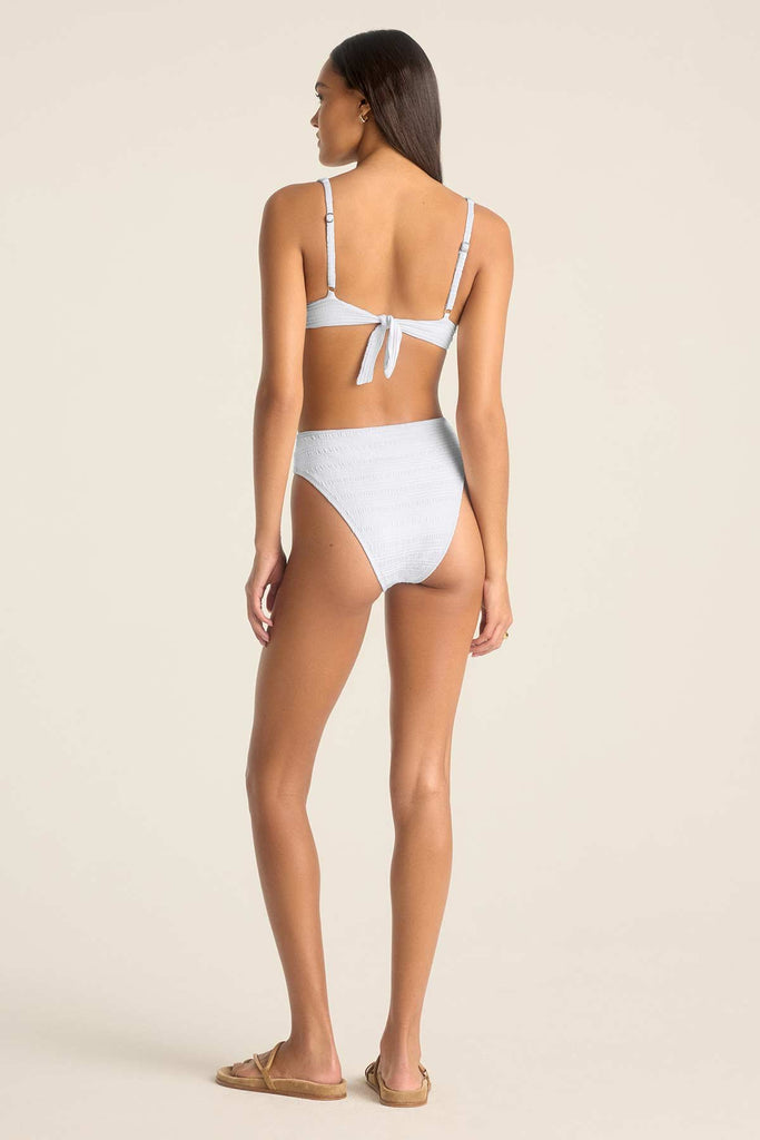 Woman turned away wearing a white bikini top and matching high waisted white swim bottoms