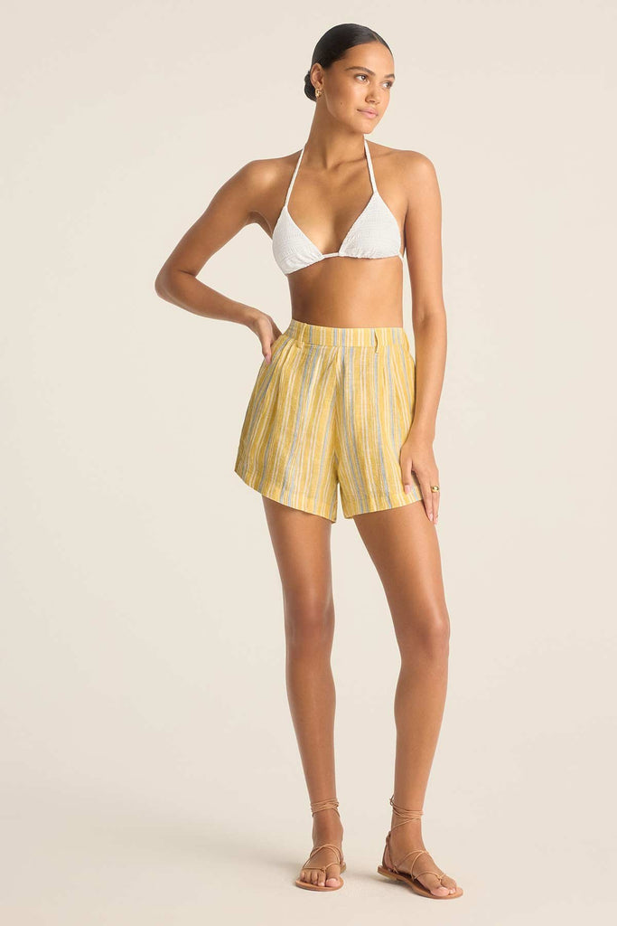 Woman wearing a white string bikini top with yellow striped beach shorts
